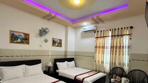 A hotel room with two beds, a ceiling fan, an air conditioning unit, and a dining area with chairs and a table. - Ngoc Nam Hotel (La Gi)