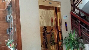 A hotel lobby with a wooden reception desk, a glass partition with a decorative design, a staircase with a wooden railing, and a potted plant. - Ngoc Nam Hotel (La Gi)