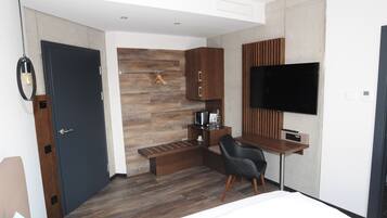 A modern hotel room with a wooden floor, a desk with a chair, a flat-screen TV, and built-in cabinets.
