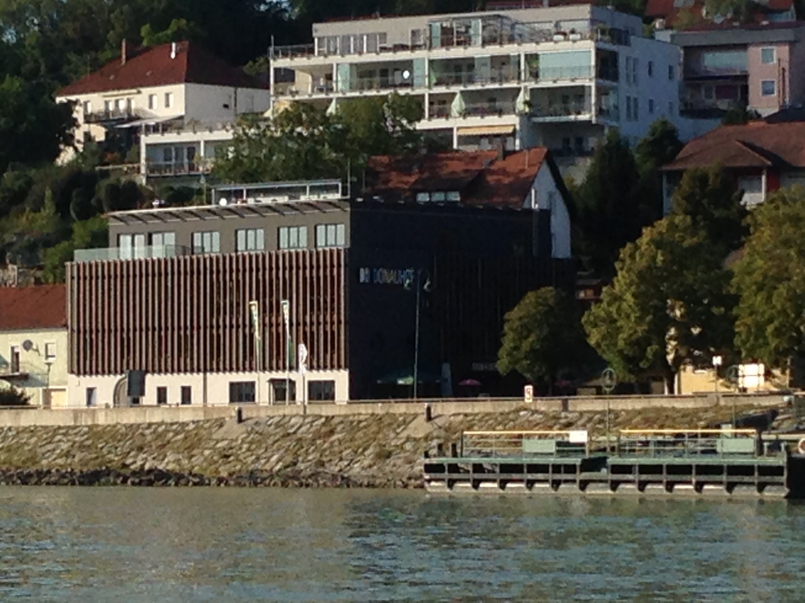 A waterfront building with a modern design, featuring a prominent vertical wooden facade and a flat roof.