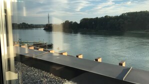 Uitzicht vanuit een raam op een rivier met een aanlegsteiger en een elektriciteitspylon in de verte.