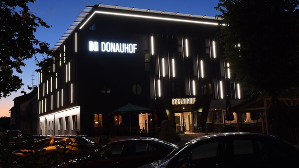 Een modern gebouw met een opvallend 'DONAUHOF' bord, voorzien van verticale lichtstroken en een plat dak.