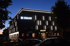 Un bâtiment moderne, reconnaissable à son grand panneau « DONAUHOF », doté de bandes lumineuses verticales et d’un toit plat.