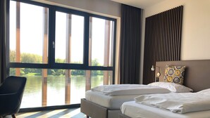 Een hotelkamer met twee bedden, een stoel en een groot raam met uitzicht op water.