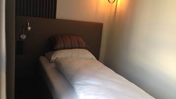A single bed with white bedding, a striped pillow, and a wall-mounted light fixture.