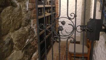 Un muro de piedra, una puerta metálica, una silla de madera y una estantería para vinos con botellas.