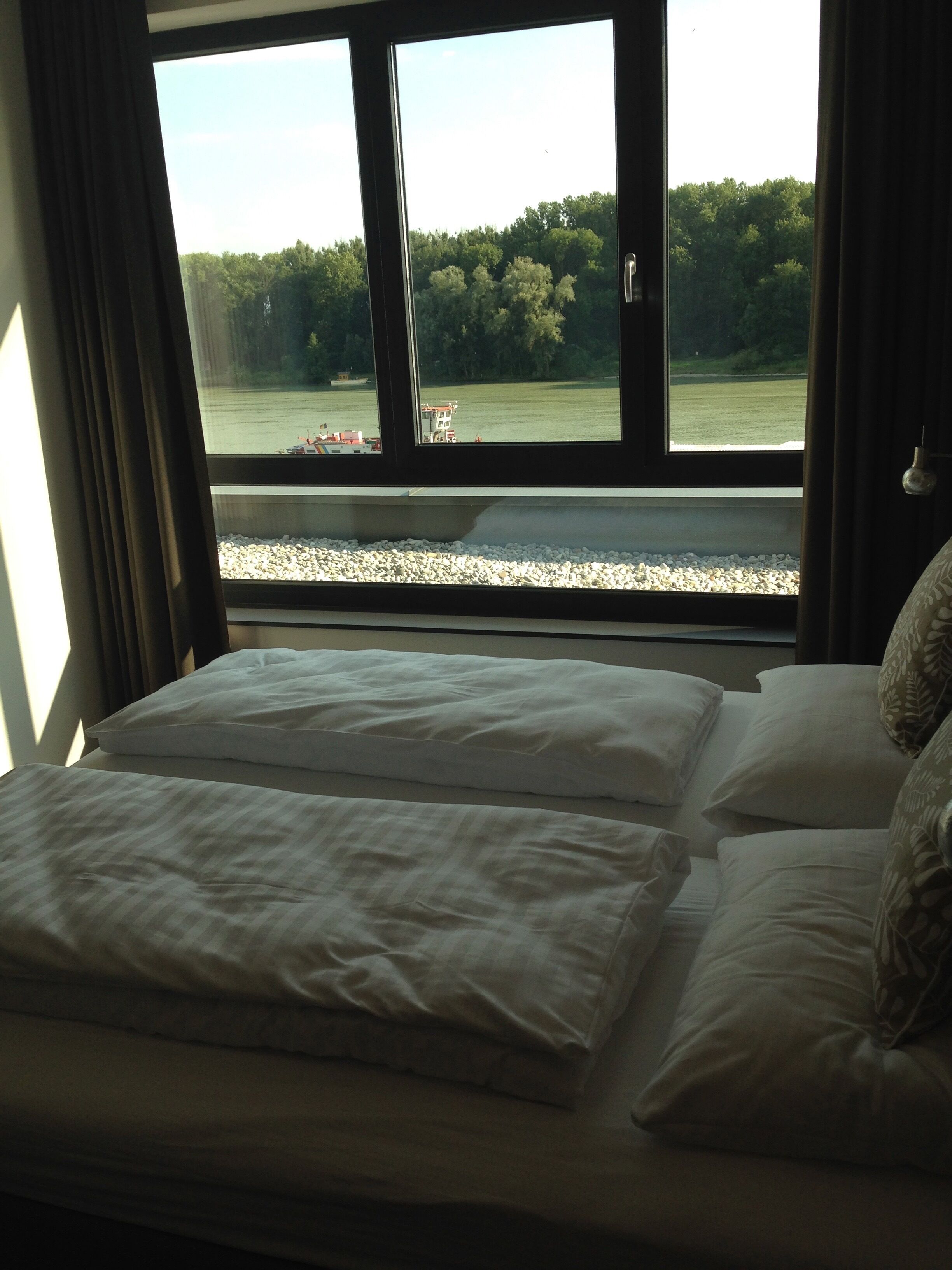 A bed with white bedding and a view of a lake and trees through a window.