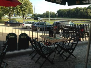 An outdoor seating area with a table and chairs, a trash bin, and a red umbrella.