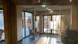 Een hotel lobby met een houten vloer, een receptiebalie, een groene fauteuil en een glazen deur die naar buiten leidt.