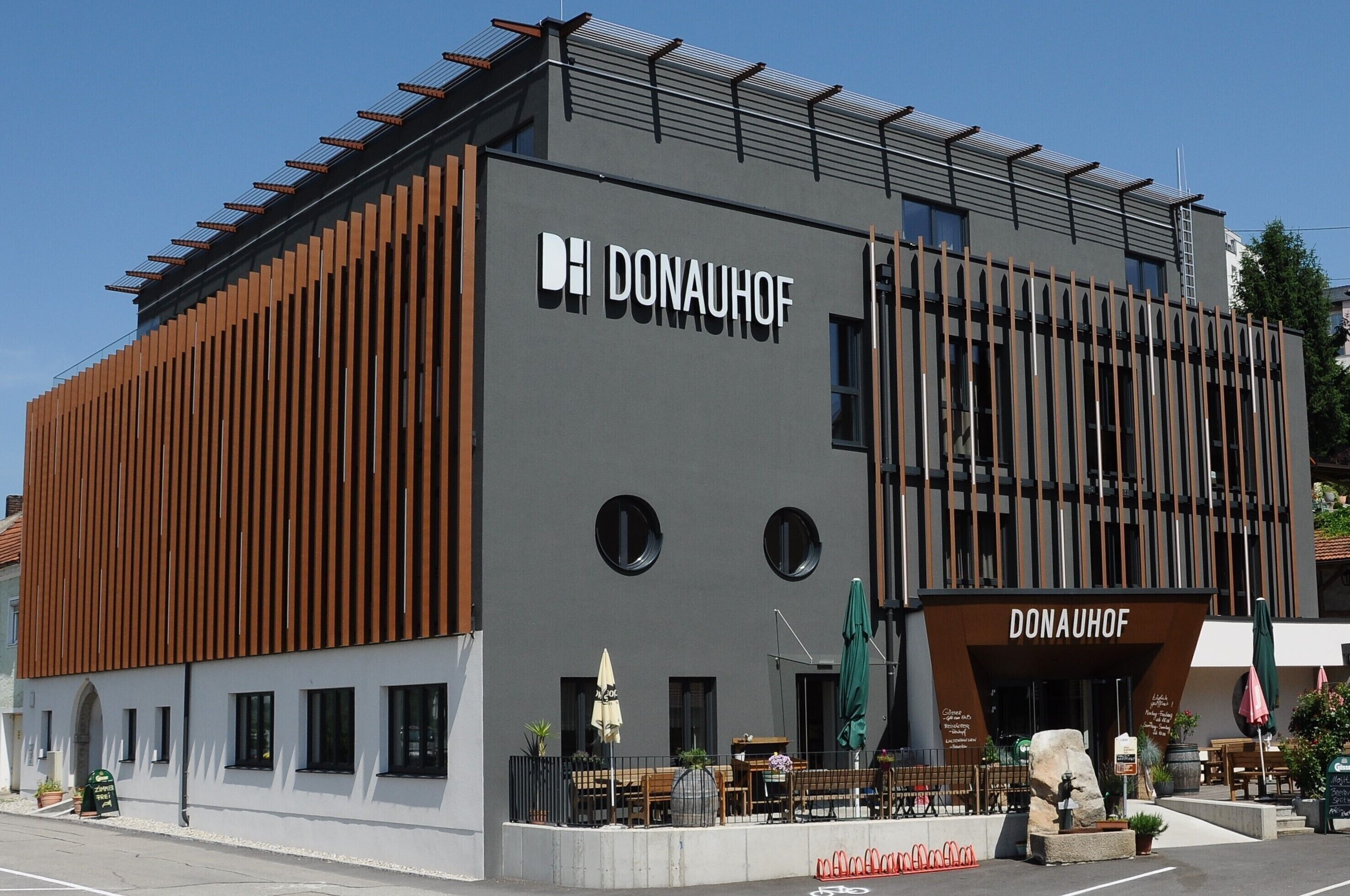 A modern building with the name "DONAUHOF" prominently displayed. It features a combination of vertical wooden slats and a grey facade.