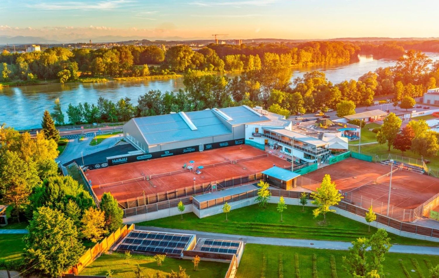 A sports complex with multiple tennis courts, a large building with a sloped roof, and solar panels.