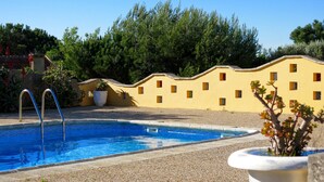 Une piscine à l’eau d’un bleu limpide, entourée de galets. On aperçoit, au fond, un bâtiment jaune avec de nombreuses fenêtres.