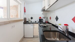 A compact kitchen with a dishwasher, microwave, stove, and sink. - FLH Garden House near Ericeira II (São João das Lampas)