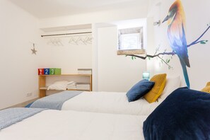 Une chambre à coucher avec un lit, une étagère où sont pliés des vêtements, une étagère fixée au mur et une fenêtre.
