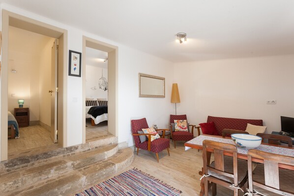 A living room with a sofa, two armchairs, a dining table with chairs, a TV, and a staircase leading to another room.