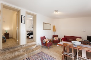 A living room with a sofa, two armchairs, a dining table with chairs, a TV, and a staircase leading to another room.