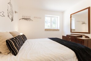 Ein Schlafzimmer mit Bett, Kommode, Spiegel und Fenster.