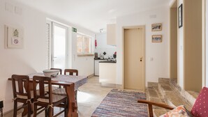 A dining area with a table and chairs, a kitchen in the background, and a staircase leading to another floor. - FLH Garden House near Ericeira II (São João das Lampas)