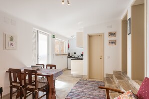 A dining area with a table and chairs, a kitchen in the background, and a staircase leading to another floor.