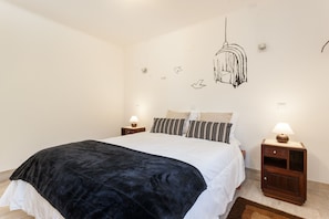 A bedroom with a bed, two nightstands, a hanging light fixture, and wall art.