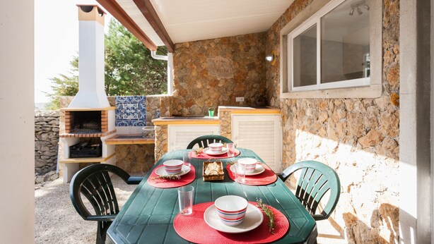 An outdoor dining area with a stone wall, a chimney, and a window. - FLH Garden House near Ericeira II (São João das Lampas)