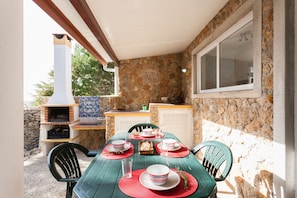Un espace extérieur aménagé pour les repas, avec un mur en pierre, une cheminée et une fenêtre.