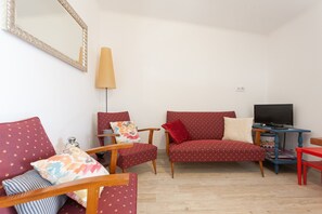 Ein Wohnzimmer mit einer Couch, Sesseln, einem Fernseher und einer Lampe.