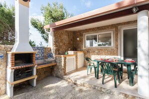 Eine Terrasse im Freien mit einer Steinmauer, einem Backofen aus Ziegeln, einem Tisch mit Stühlen und einem Fenster.
