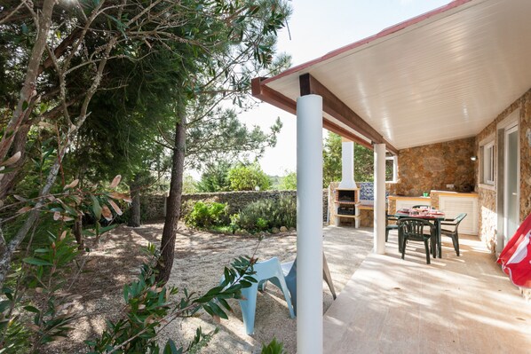 A covered outdoor patio with a stone wall, a barbecue area, and a table with chairs.
