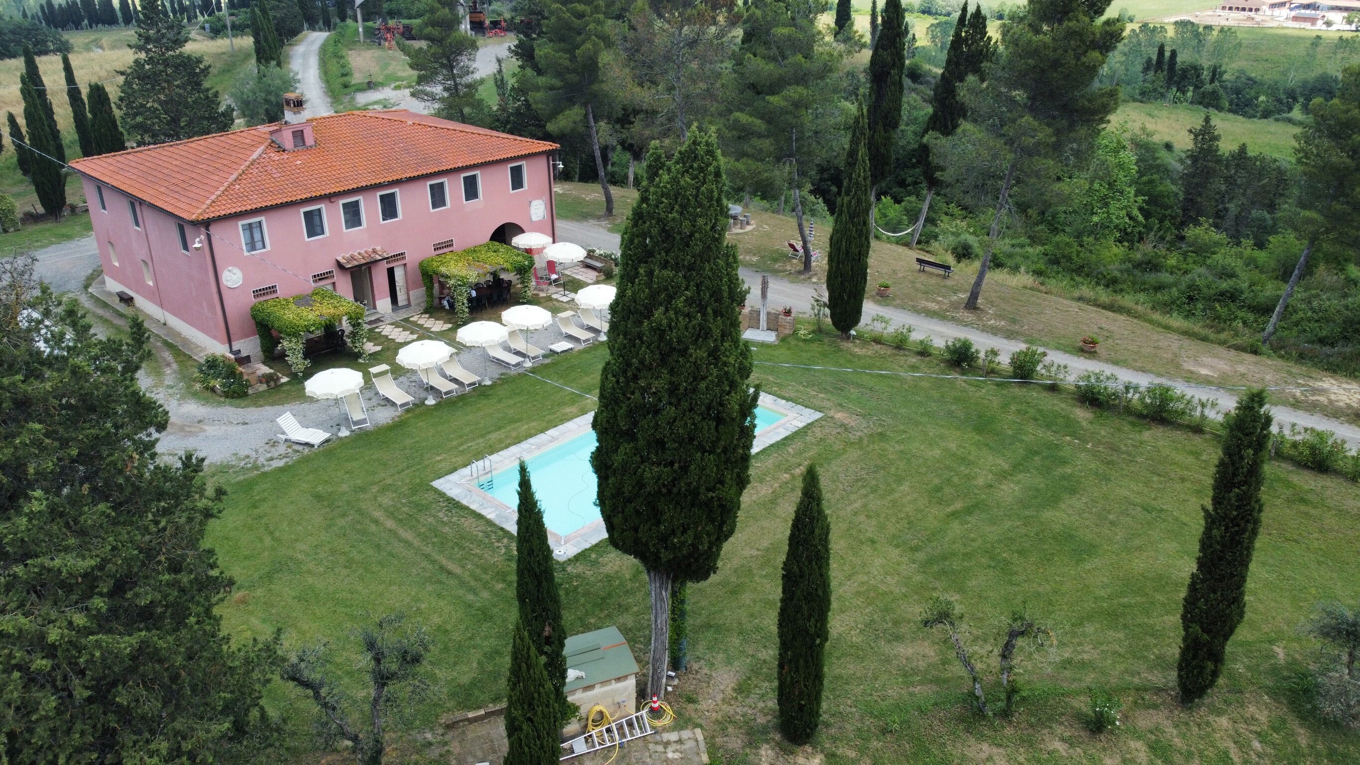 A pink villa with a swimming pool, surrounded by a well-maintained lawn and tall cypress trees.