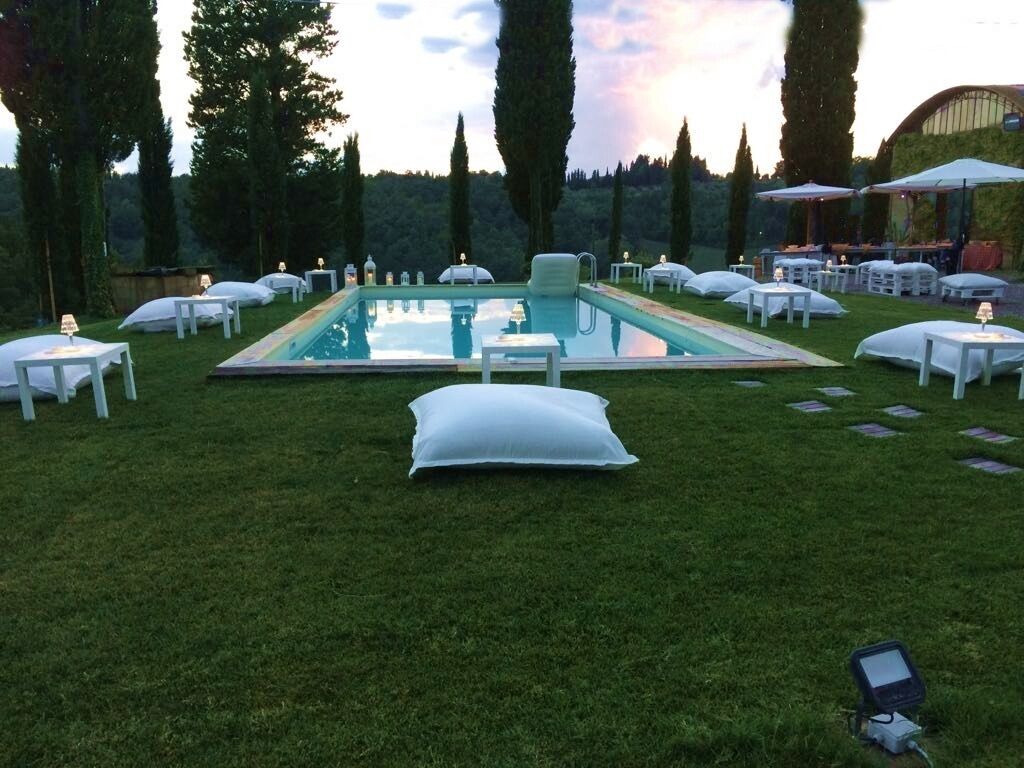 An outdoor pool area with lounge chairs and tables, surrounded by trees.