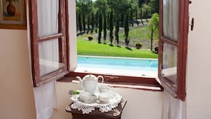 A view through an open window with a table set for tea, overlooking a pool and a grassy area with trees.