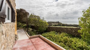 Un bâtiment en pierre doté d’une terrasse carrelée de tuiles rouges, d’un mur en pierre et offrant une vue sur la mer.