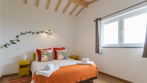 Une chambre à coucher avec un lit, une fenêtre, une table de chevet et une lampe fixée au mur.