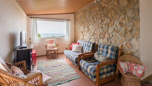 Un salon chaleureux avec un mur en pierre, un plafond en bois, un canapé, un fauteuil et un téléviseur.