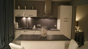 Une cuisine moderne dotée d’un îlot central, d’appareils électroménagers intégrés et d’un plan de travail de couleur sombre.