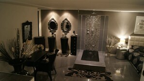 Una sala de estar moderna con comedor, dos espejos grandes, una chimenea y un detalle decorativo en la pared.