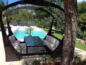 Un fauteuil suspendu, de type hamac, offrant une vue sur une piscine et un jardin.