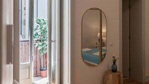 Una stanza con un letto, uno specchio, una pianta in vaso e uno sgabello di legno.