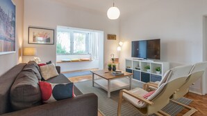 Een moderne woonkamer met een bank, salontafel, fauteuil, televisie en decoratieve planten.