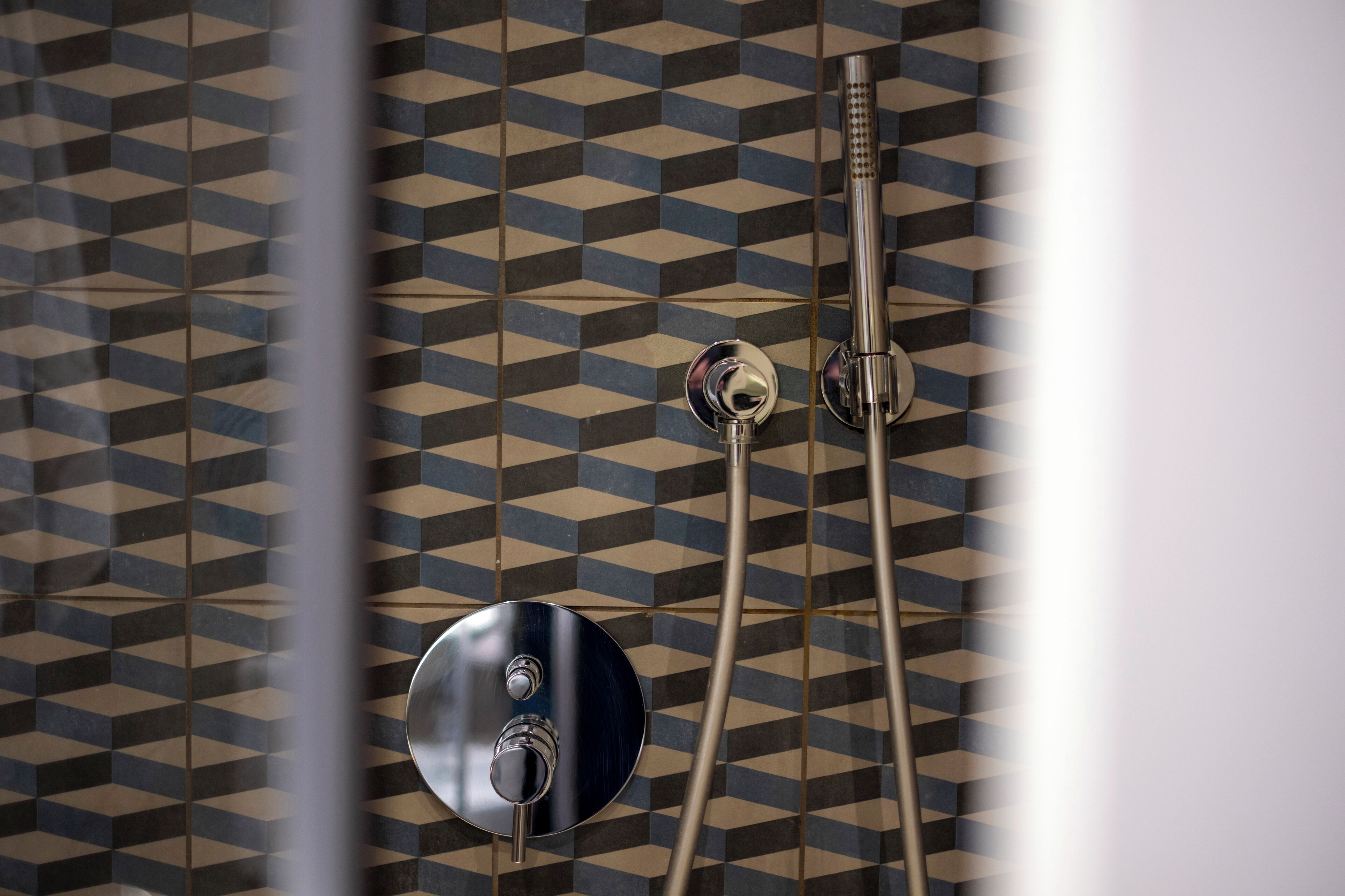 Casa de banho com parede revestida de azulejos com padrão geométrico e chuveiro moderno.
