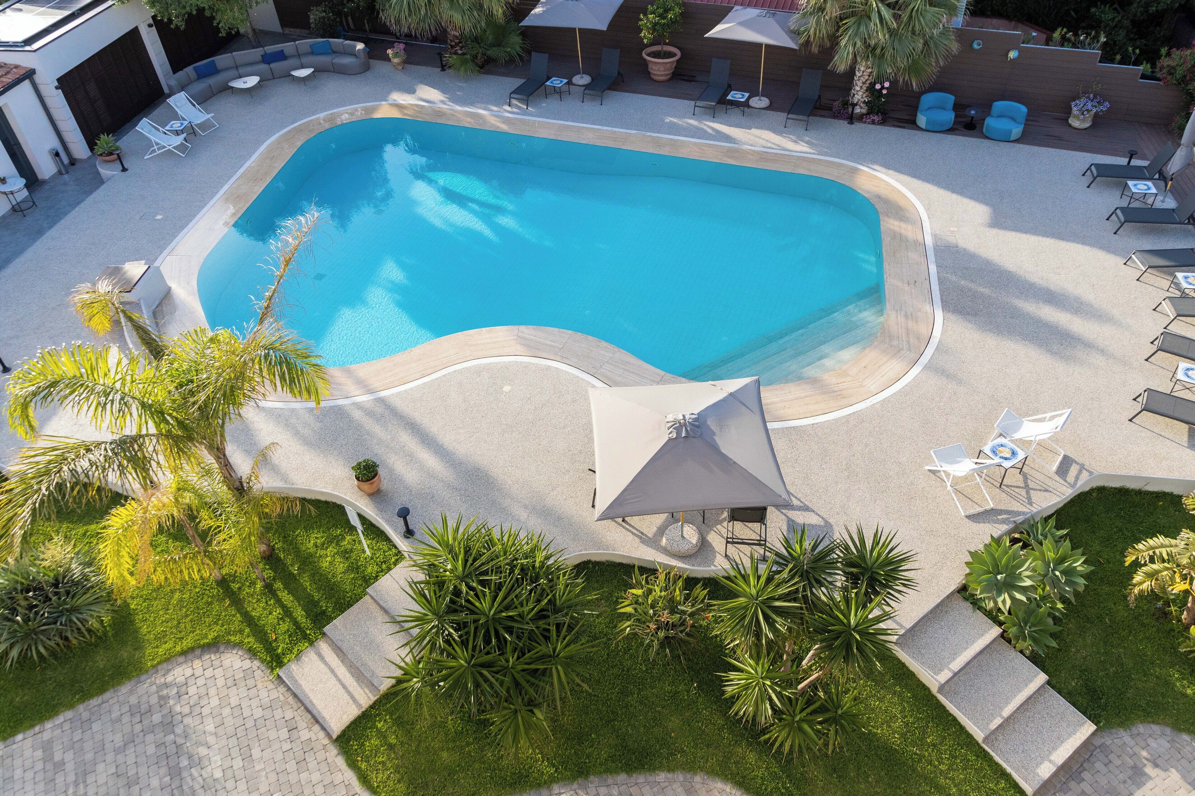 Vue aérienne d’une piscine entourée de chaises longues et d’un petit jardin.
