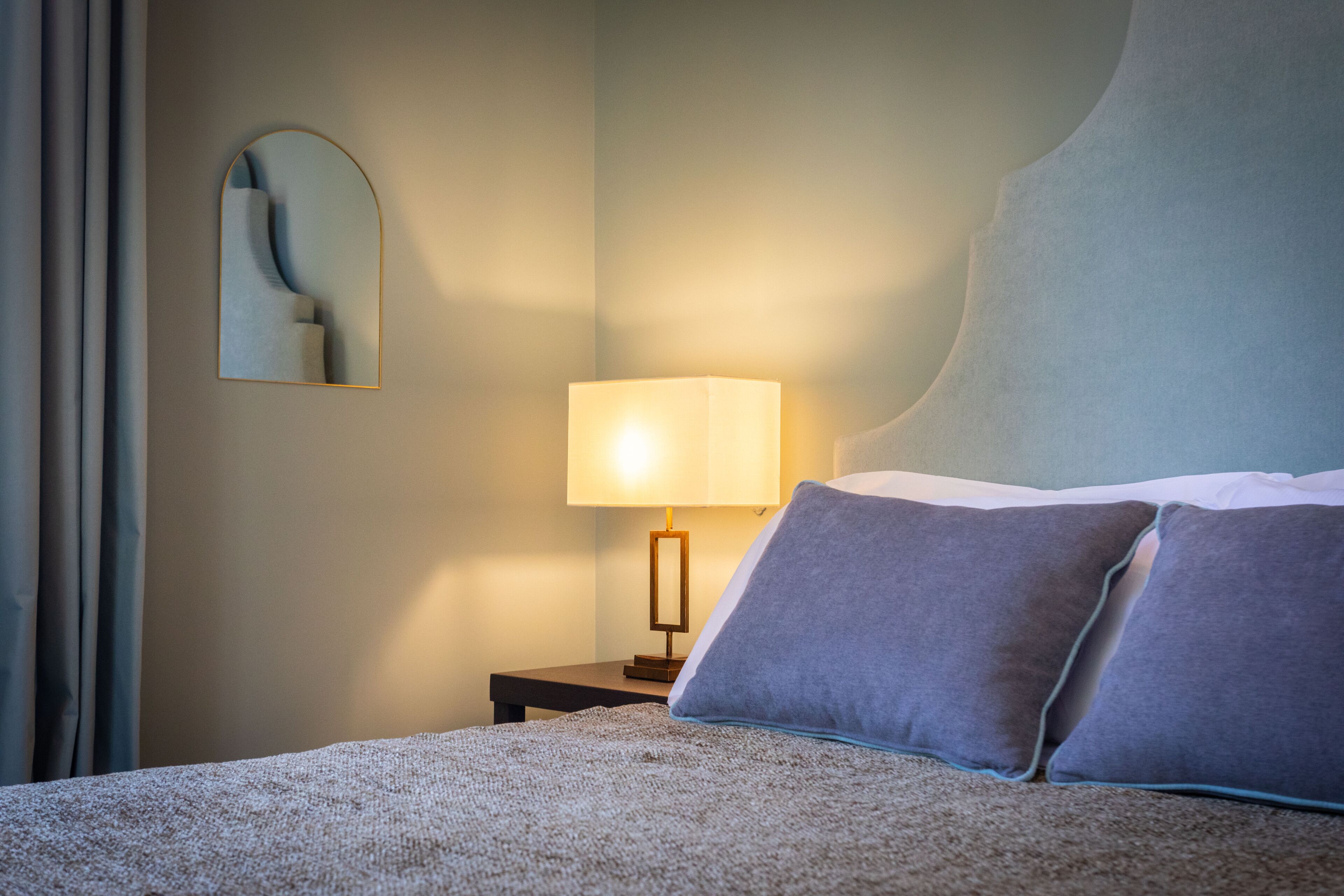 A neatly made bed with a textured blanket, a bedside lamp, and a wall-mounted mirror.