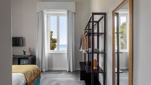 A modern hotel room with a bed, a TV, a desk, a bookshelf, and a large window with curtains. - Villa Masetta - Luxury Suite (Palermo)