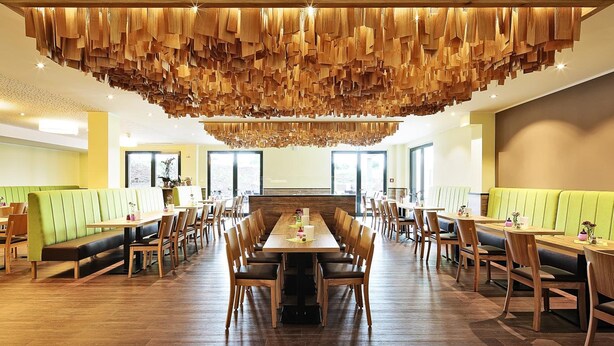 Un vaste espace dédié à la salle à manger, avec une longue table en bois et de nombreux coins repas, agrémenté d’un plafond en bois au design original.