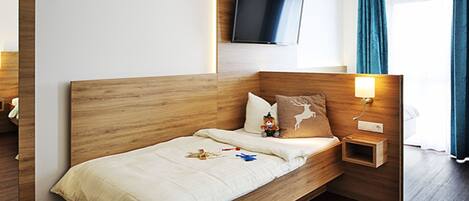 Une chambre d’hôtel moderne avec un lit en bois, un téléviseur fixé au mur et une table de chevet avec une lampe.