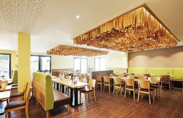 Un restaurante con mesas y sillas de madera, un banco acolchado verde y una lámpara colgante singular.