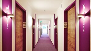 Un couloir d’hôtel aux murs violets et aux portes numérotées de 211 à 216.