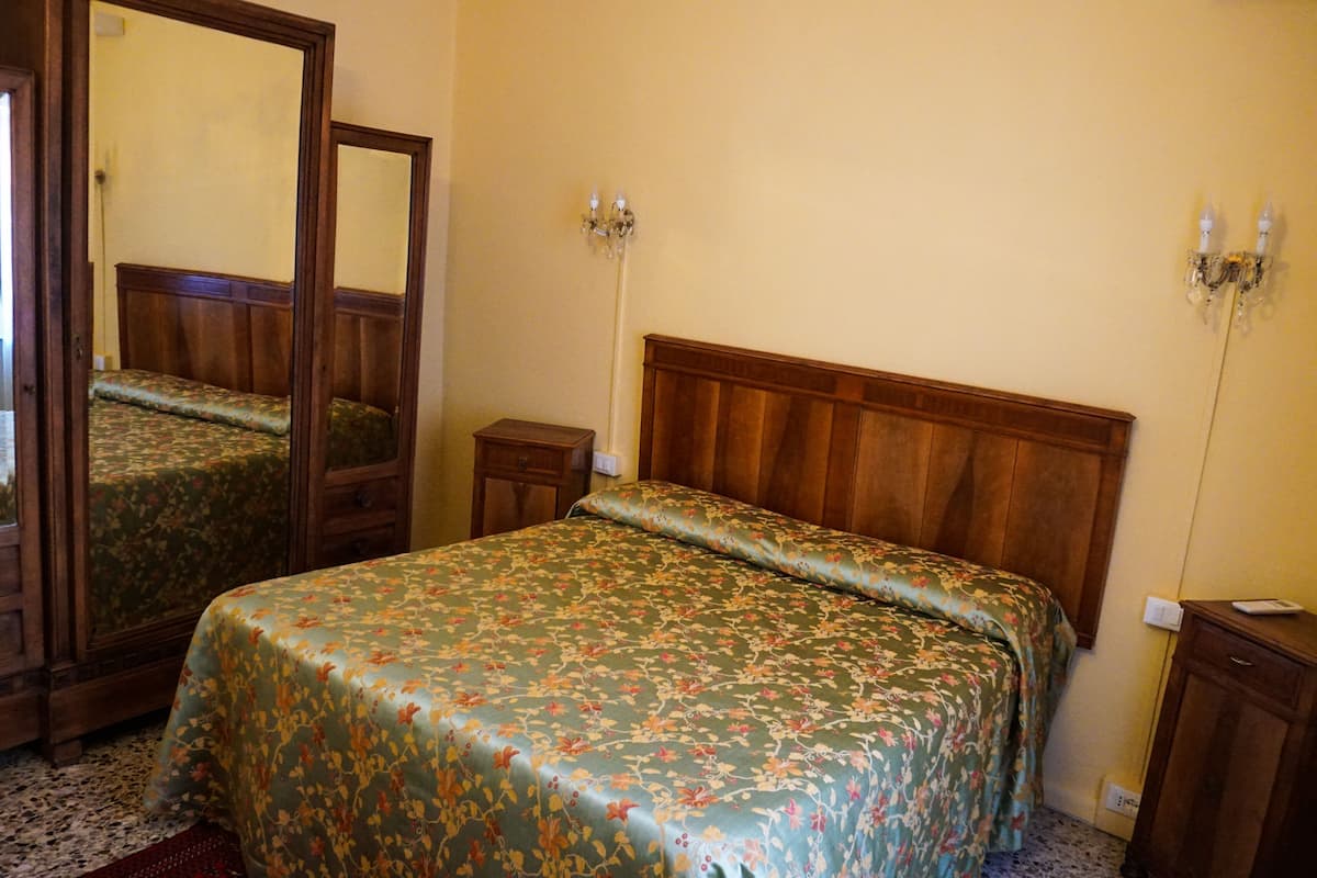 A bedroom with a wooden bed, a mirror, a nightstand, and a wall-mounted light fixture.