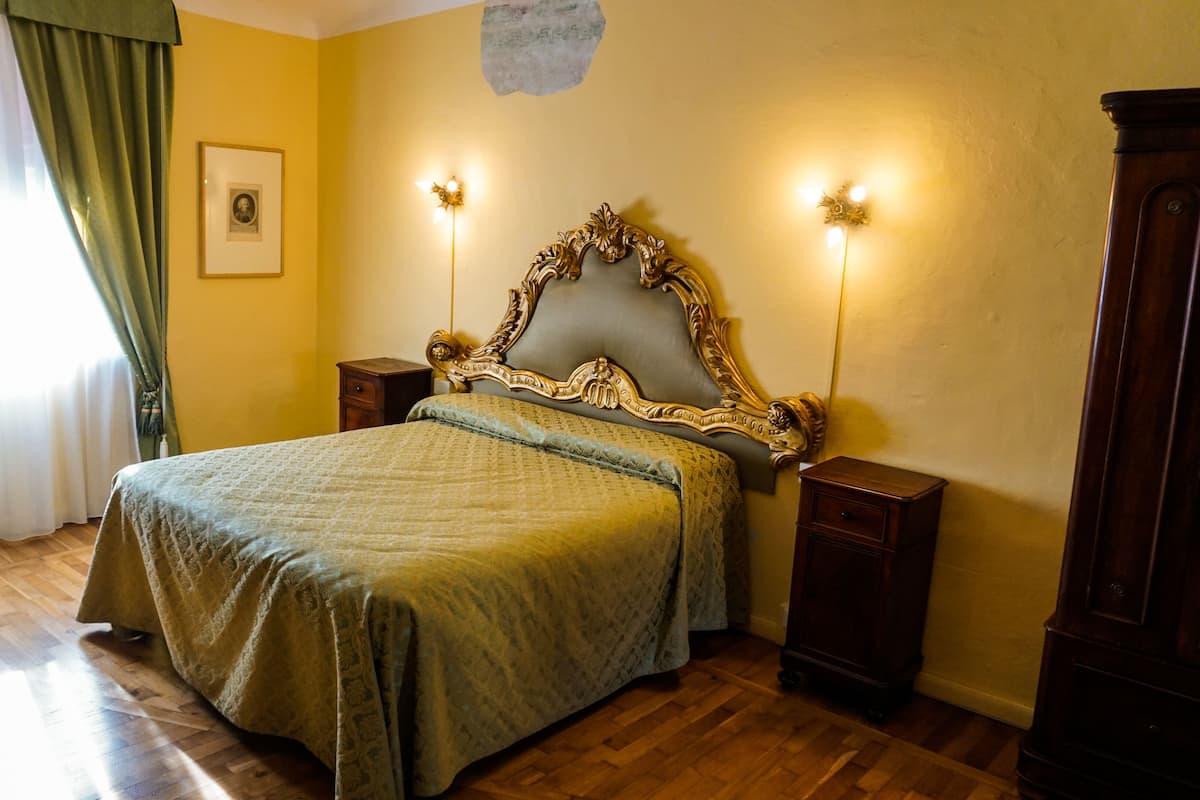 A bedroom with a bed, wooden nightstands, a dresser, a framed picture on the wall, and a window with curtains.